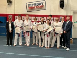 Line-up of adults from Star Martial Arts in Milton Keynes in their taekwondo suits with certificates for new belt achievements