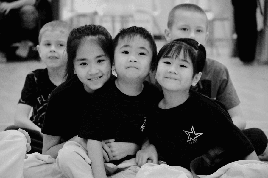 Group of young children in Star Martial Arts tees huddled together like a family. Black & white pic.